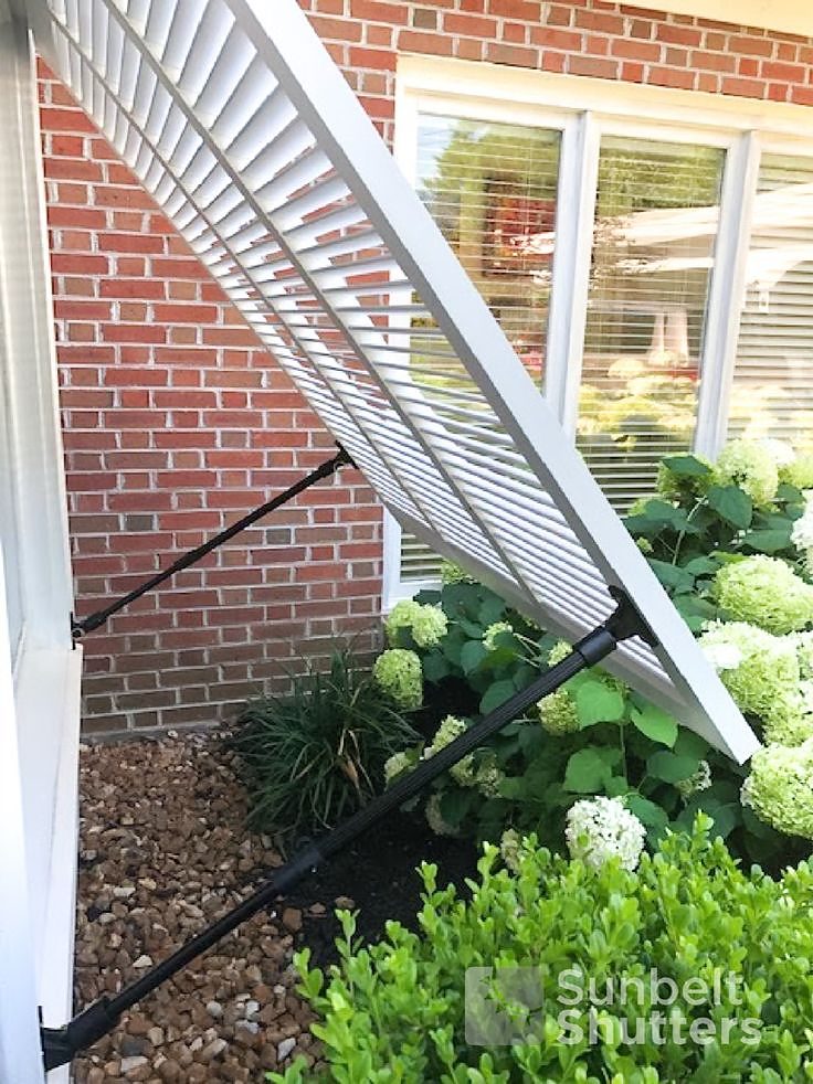 Adjustable support arms holding a white Bahama shutter open over a window