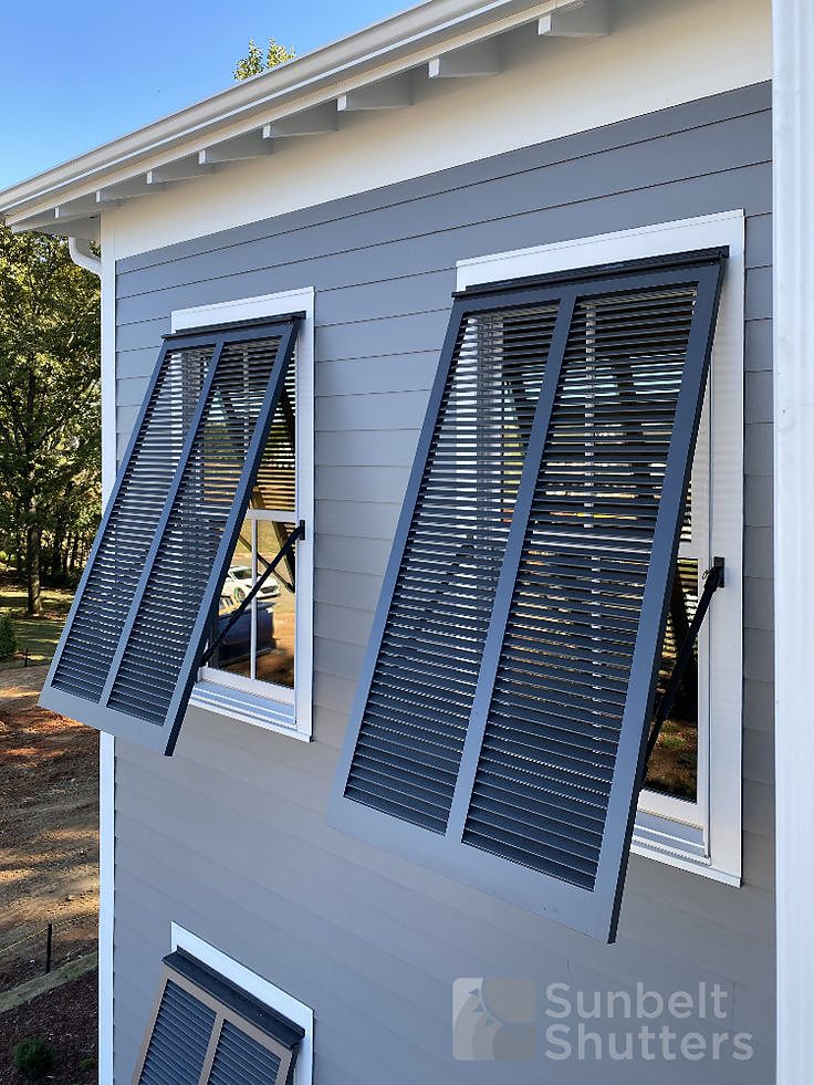 Dark gray Classic Bahama exterior shutters propped open over windows on gray siding
