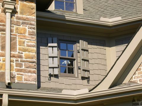 Sage-green open board and batten shutter with an S-scroll shutter dog, on a stone and shingle gable.