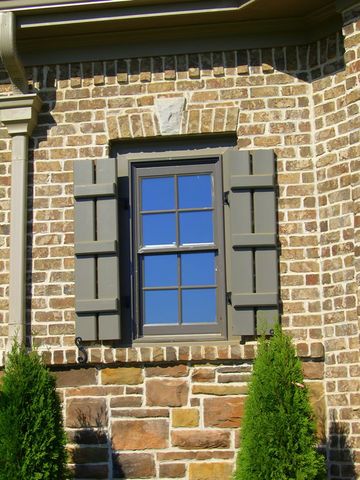 Olive open board and batten shutters on a stone facade, held with shutter dogs at the sills.