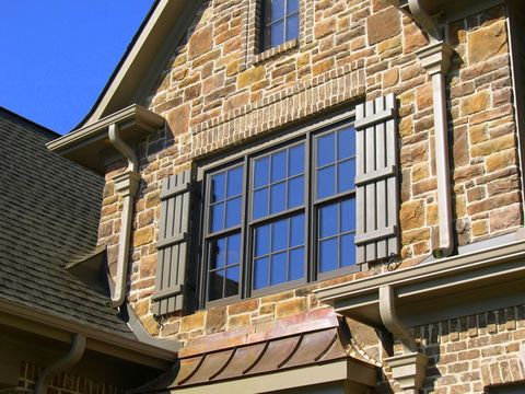 Olive open board and batten shutters flanking a wide window on a stone gable, copper bay roof below.