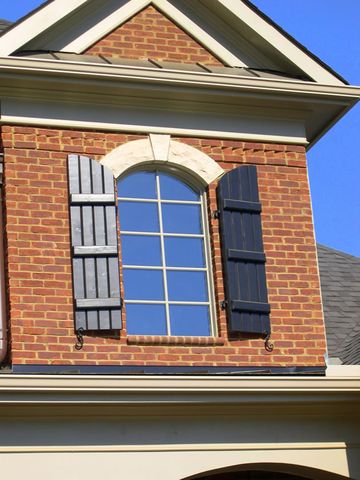Black open board and batten shutters with arched tops on an arched window, red brick.