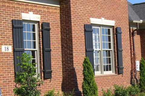 Black closed board and batten shutters on a brick home, with shutter dogs at the sills.