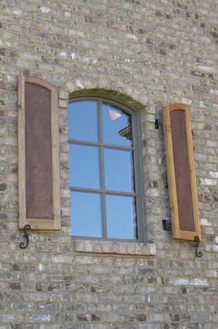 Stained flat panel shutters with rough-sawn cedar panels on an arched window, with S-scroll shutter dogs.