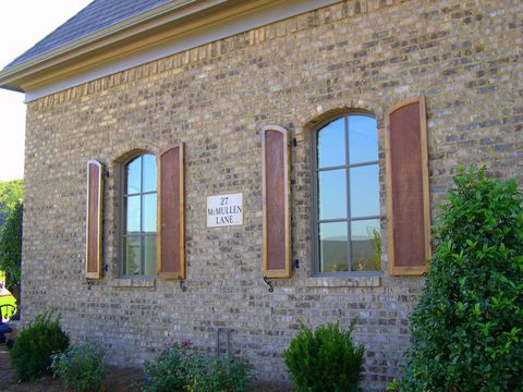 Stained arch-top flat panel shutters with rough cedar panels on a pair of arched windows, tan brick.