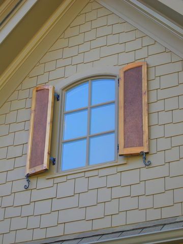 Stained arch-top flat panel shutters with rough cedar panels on a shingled gable.