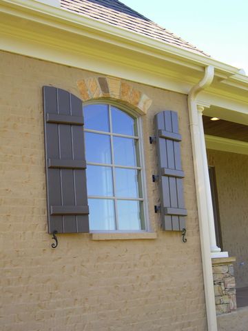 Taupe closed board and batten shutters with arched tops on a stucco home, with shutter dogs.