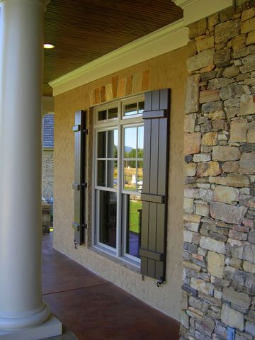 Taupe closed board and batten shutters on a porch window, beside a stacked-stone column.