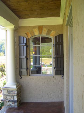 Taupe closed board and batten shutters with arched tops on a covered porch window.
