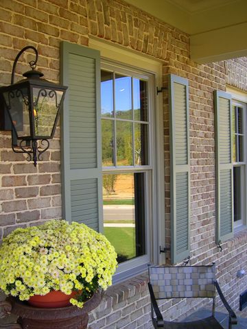 Sage Charleston louvered shutters on a brick home, with a gas lantern at the entry.