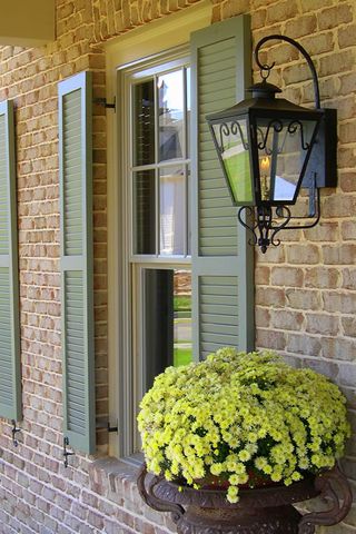 Sage Charleston louvered shutters beside a copper gas lantern, brick home.