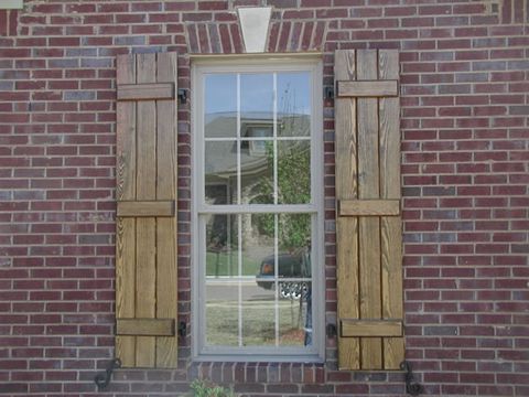 Natural stain-grade closed board and batten shutters on red brick, with shutter dogs.