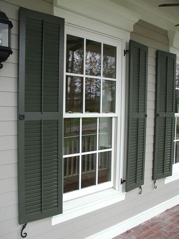 Dark green Charleston louvered shutters on lap siding, hung on hinges with S-scroll shutter dogs.