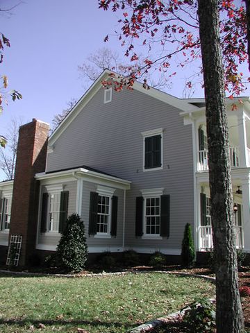 Grey two-story home with dark green louvered shutters and a brick chimney.