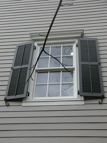 Dark green louvered shutters on grey lap siding, with shutter dogs at the sill.