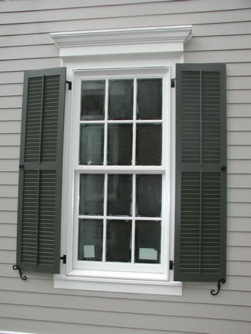 Dark green Charleston louvered shutters with S-scroll shutter dogs, white trim, grey siding.