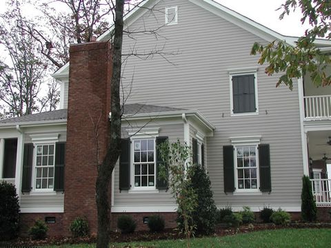 Two-story home with dark green louvered shutters and a brick chimney, fall color.