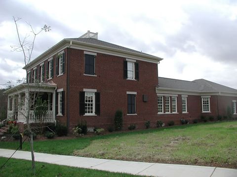 Red brick two-story Colonial with black louvered shutters on every window.
