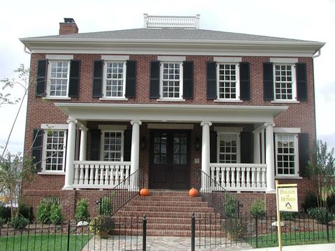 Red brick Federal-style show home with black louvered shutters and a columned porch.
