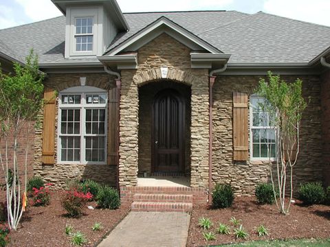 Natural stain-grade board and batten shutters on a stone cottage with an arched entry.