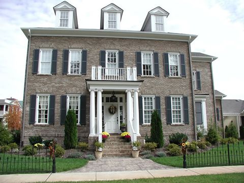 Three-story stone Georgian with black louvered shutters and dormers, columned entry.