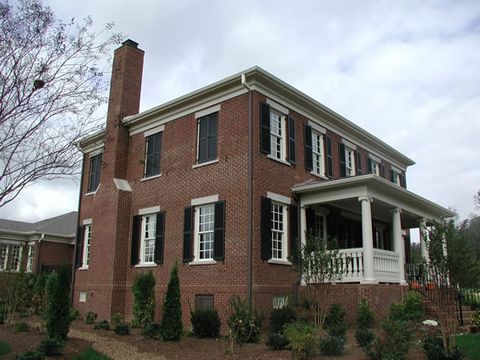 Two-story brick home with black louvered shutters and a side porch.
