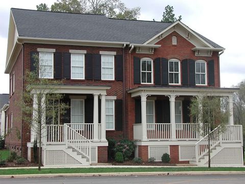Red brick two-story with black louvered shutters and a full-width front porch.