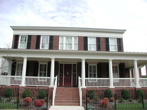 Red brick two-story with black louvered shutters and a deep front porch.