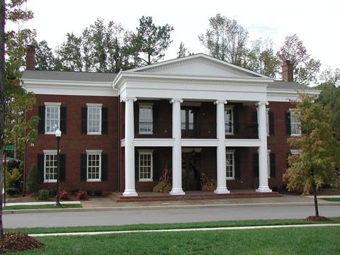 Red brick Greek Revival with black louvered shutters and two-story white columns.