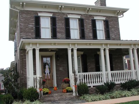 Dark brick two-story with black louvered shutters over a covered porch.