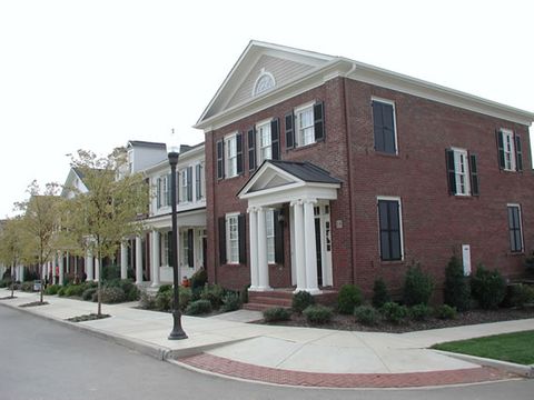 Red brick two-story with black louvered shutters and a pedimented entry, streetscape view.