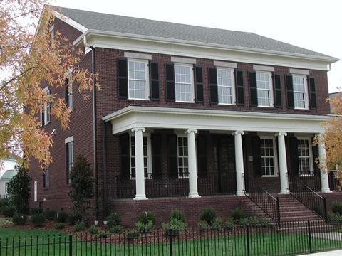 Dark brick two-story with black louvered shutters and a columned front porch.