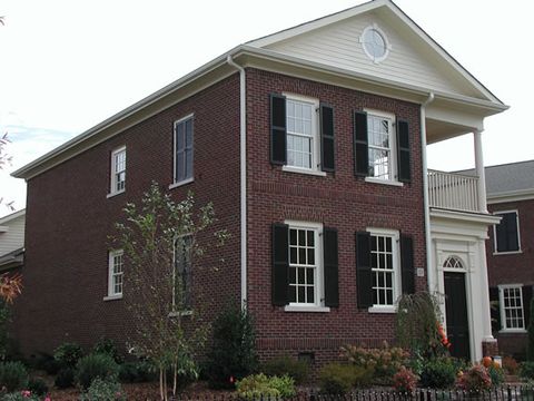 Brick two-story with black louvered shutters and a side entry portico.