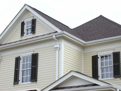 Dark louvered shutters on a cream clapboard home, gable and side windows.