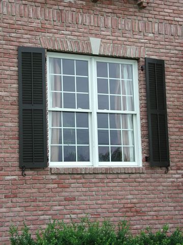 Black louvered shutters on a pink brick home, with shutter dogs at the sills.