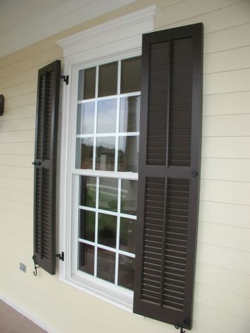 Dark brown louvered shutters on cream siding, with shutter dogs.
