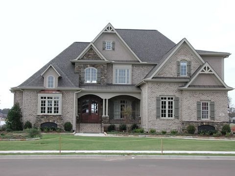 Brick and stone home with sage open board and batten shutters on the front windows and gables.