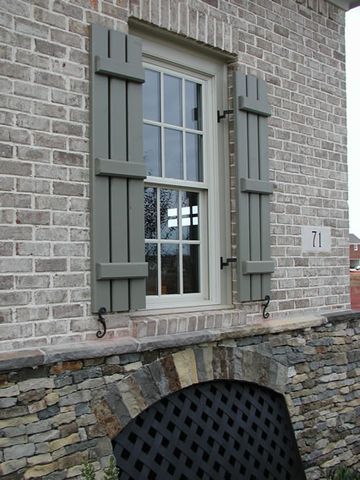 Sage open board and batten shutters on brick over a stone foundation, with shutter dogs.