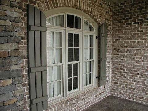 Sage open board and batten shutters flanking an arched porch window, brick and stone.