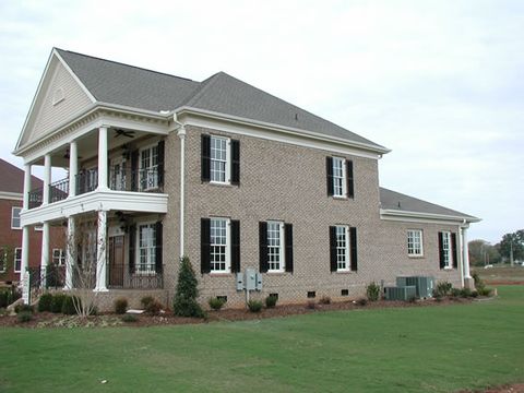 Tan brick two-story with black louvered shutters and a double porch with iron railings.
