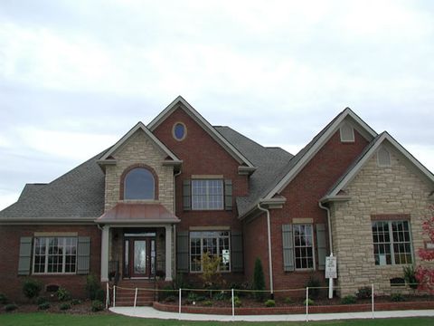 Brick and stone home with dark open board and batten shutters and an arched entry.