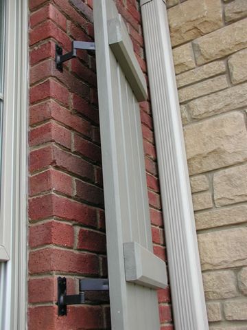 Close-up of a board and batten shutter hung on strap hinges and pintles, brick and stone corner.