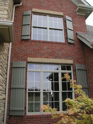Sage closed board and batten shutters on a two-story brick bay.