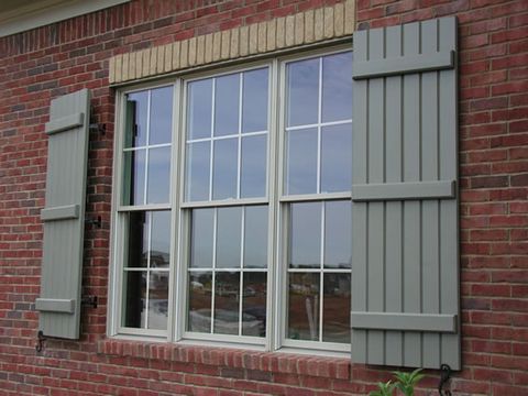 Sage closed board and batten shutters flanking a wide double window in red brick, with shutter dogs.