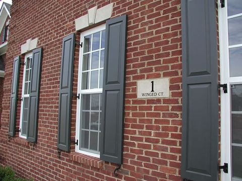 Charcoal flat panel shutters on red brick with hinges and shutter dogs.