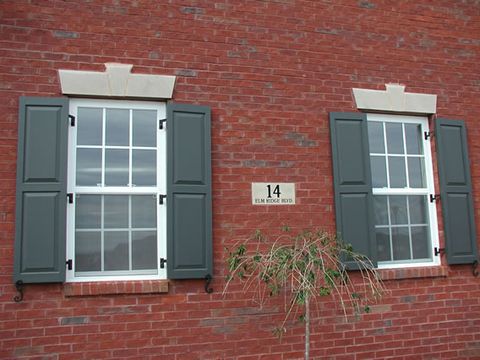 Charcoal flat panel shutters on red brick, hung on hinges with shutter dogs.