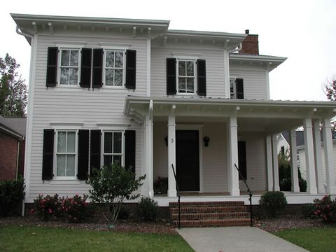 White farmhouse with black louvered shutters and a wrap-around porch.
