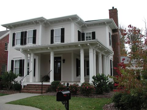 White two-story home with black louvered shutters and a columned front porch, corner view.