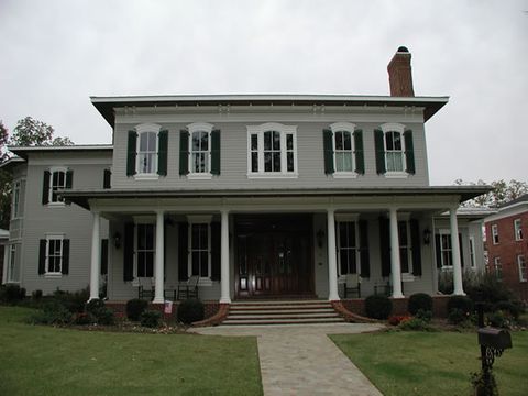 Grey Italianate-style home with dark green louvered shutters and a full-width porch.