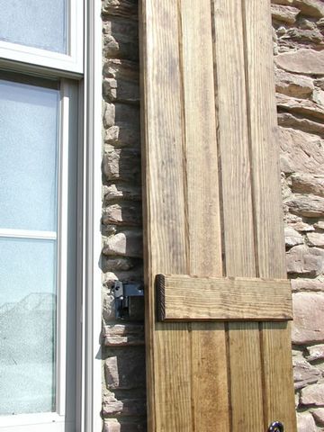 Close-up of a natural stain-grade board and batten shutter on a stacked-stone wall.